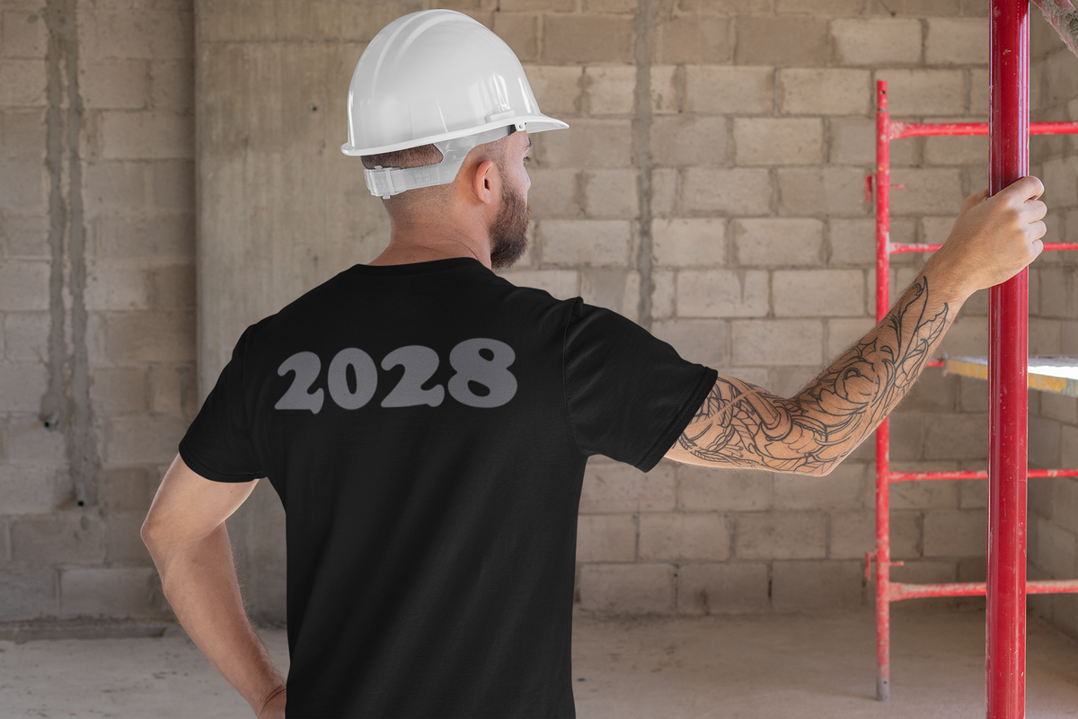 A man in a black 2028 Back Print Apparel Concept tee, wearing a hard hat, in a construction setting.