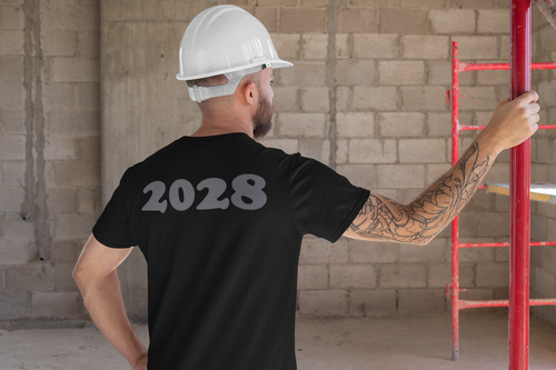 A man in a black 2028 Back Print Apparel Concept tee, wearing a hard hat, in a construction setting.