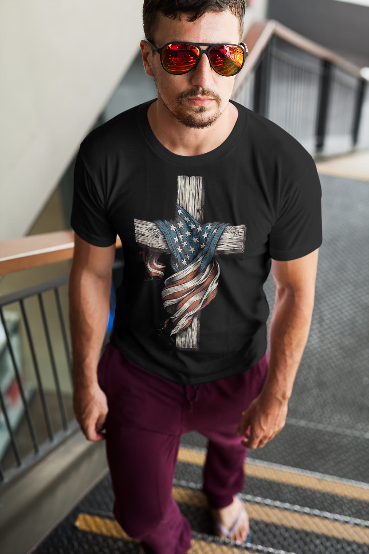 American Flag On The Cross Style t-shirt worn by a man standing on stairs, showcasing patriotic values and faith.