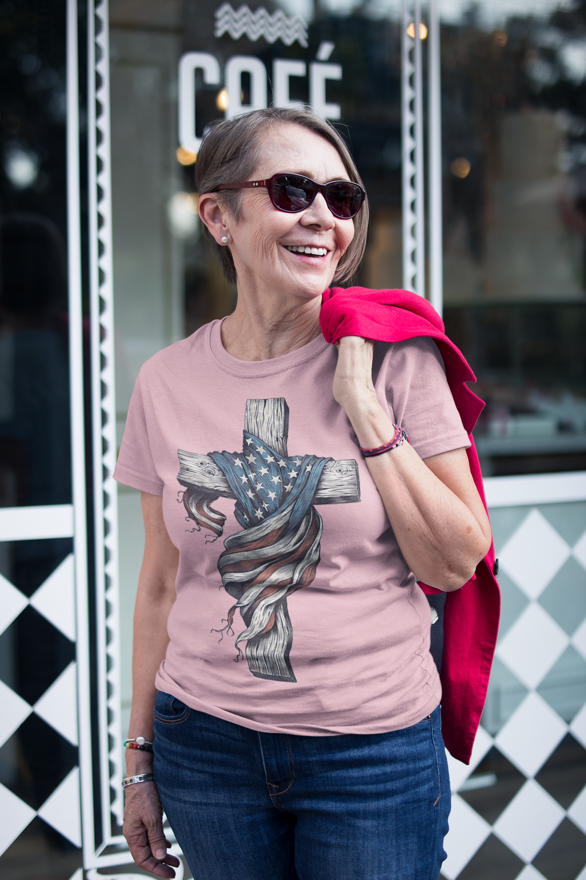 Woman wearing American Flag On The Cross Style t-shirt with sunglasses outside a café.