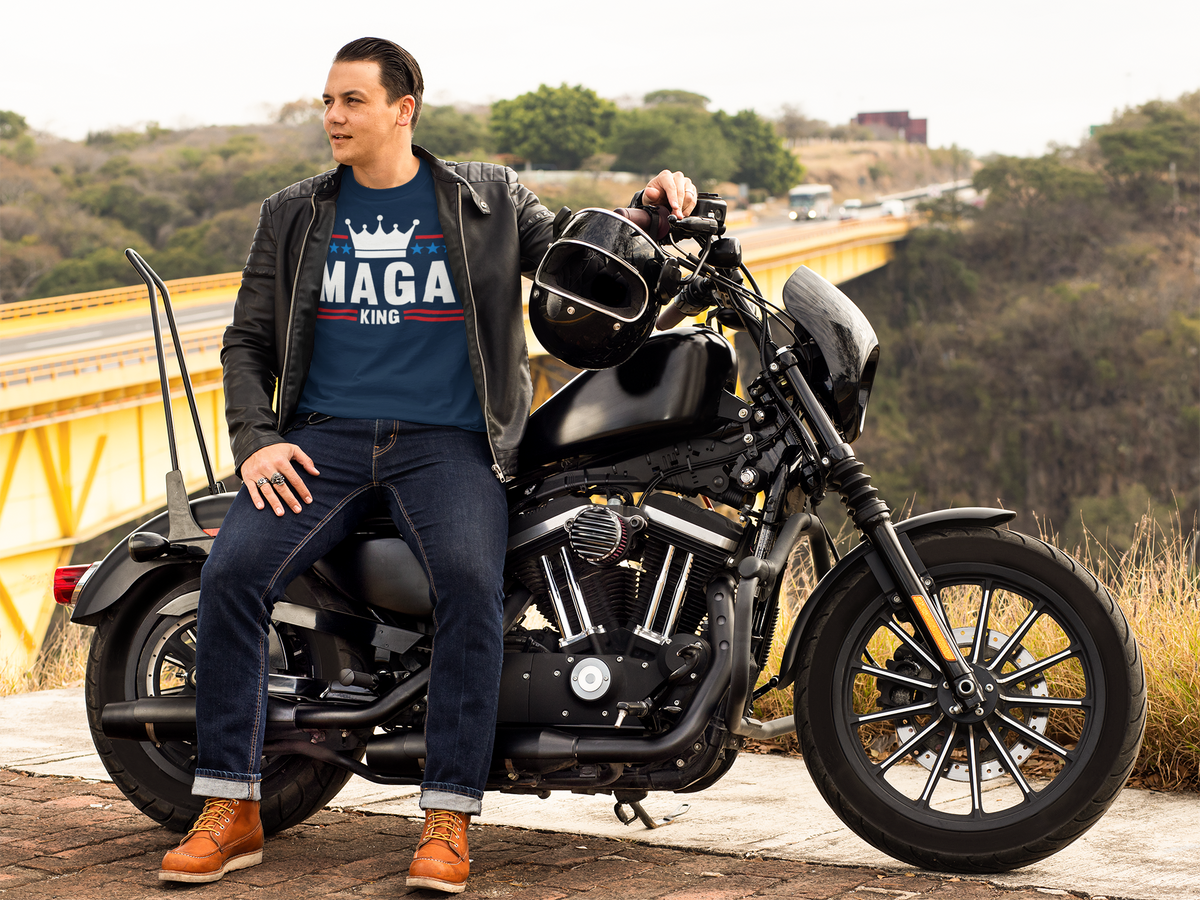 Man wearing MAGA King American Pride Shirt sitting on a motorcycle with a scenic background.