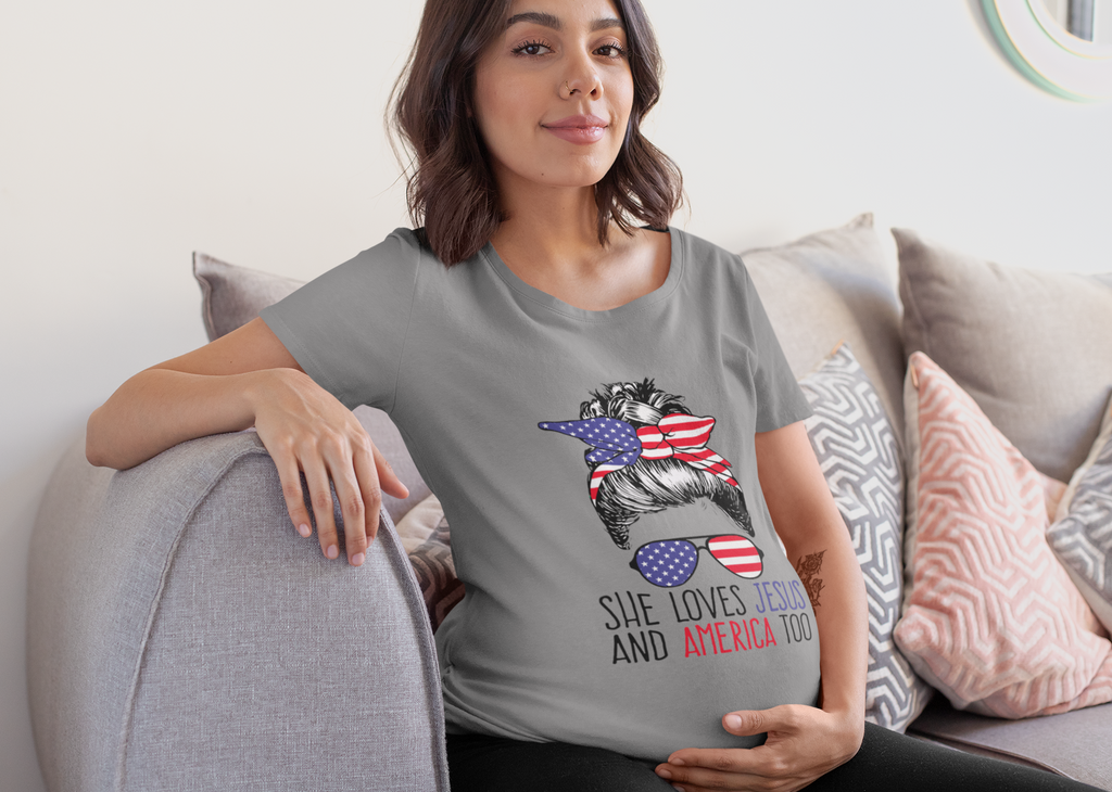Woman wearing a gray t-shirt with the design "She Loves Jesus And America Too" sitting on a couch.