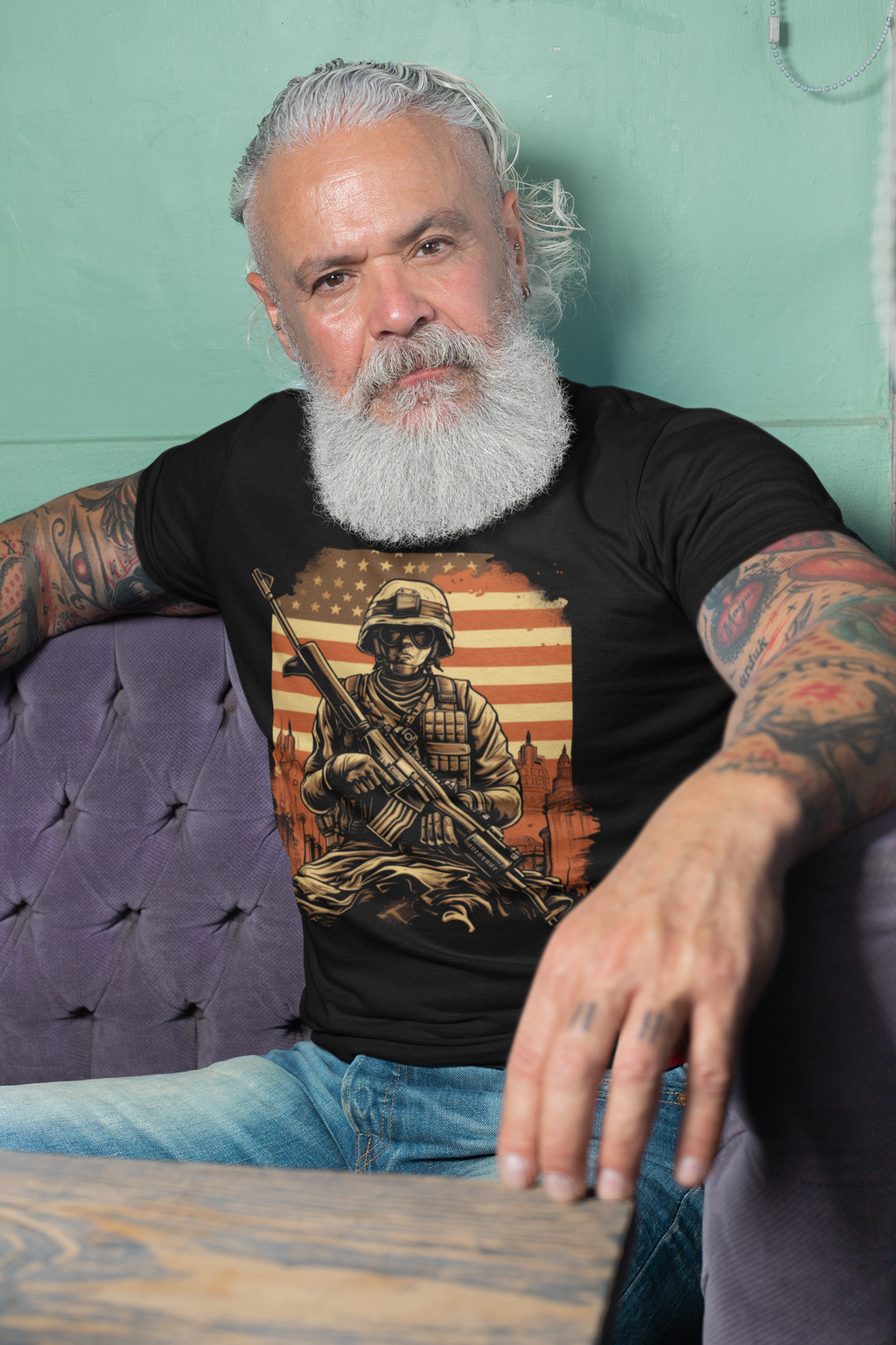 Soldier Against American Flag And City graphic tee worn by a bearded man seated on a couch.