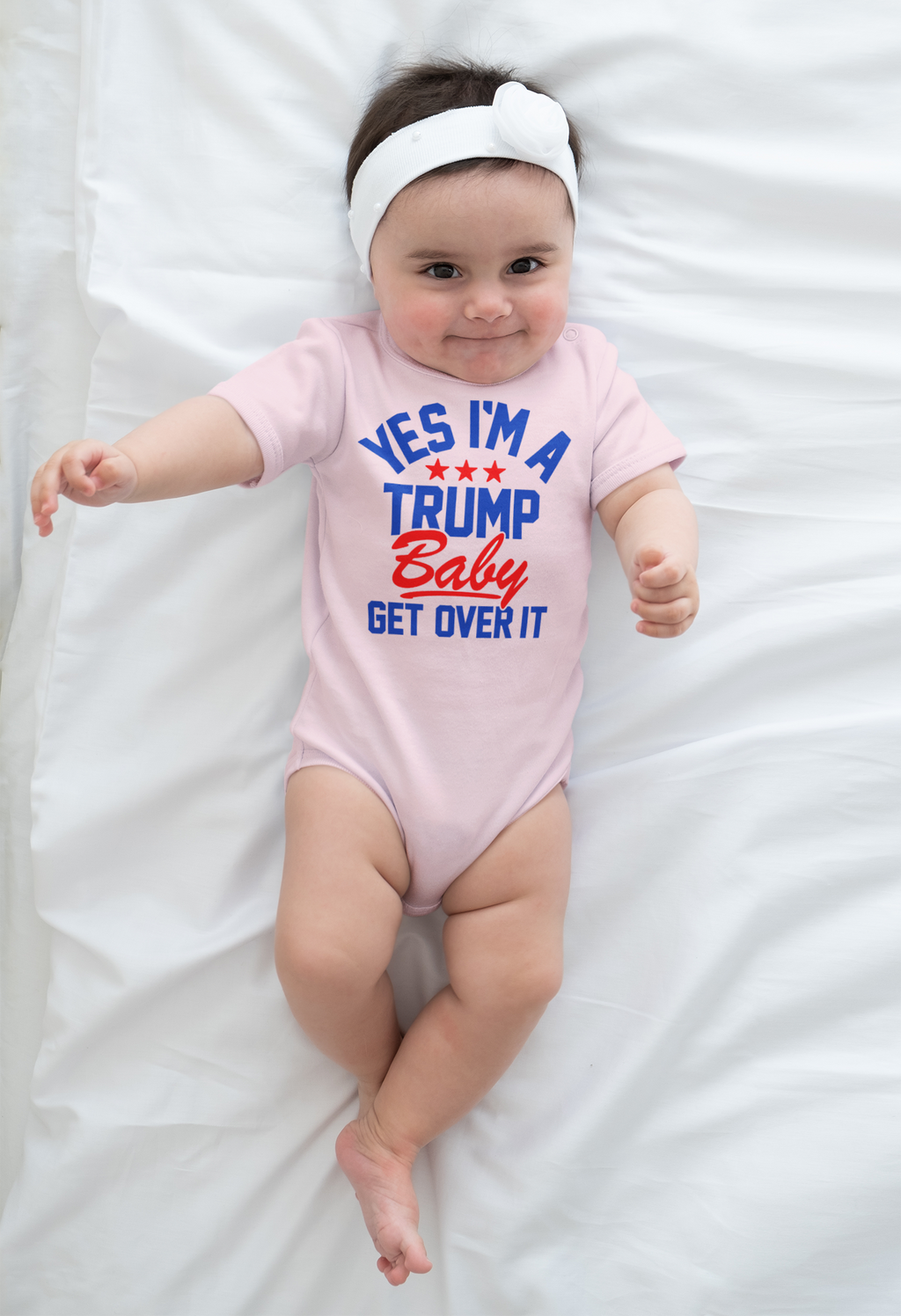 Yes I am A Trump Baby Onesie Art displayed on a baby wearing a pink onesie with a cute headband on a white sheet.