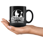 Hand holding Freedom Isn't Free Patriotic Graphic Tee mug with silhouette design.
