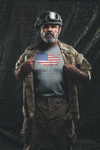 Man in military gear showcasing America Home Of The Free Because Of The Brave shirt with American flag print.