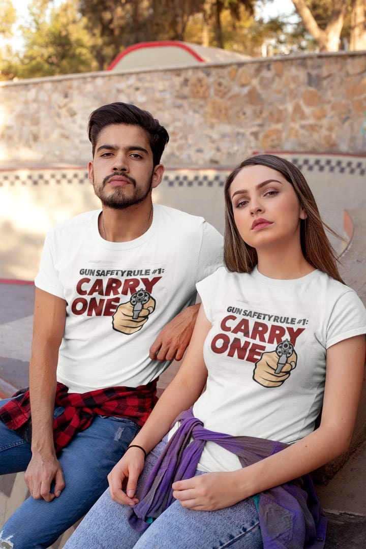 Two people wearing 'Gun Safety Rule Always Carry One' graphic t-shirts outdoors.