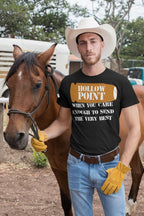 Man in a cowboy hat and gloves wearing a 'Hollow Point When You Care Enough To Send The Very Best' t-shirt standing by a horse.
