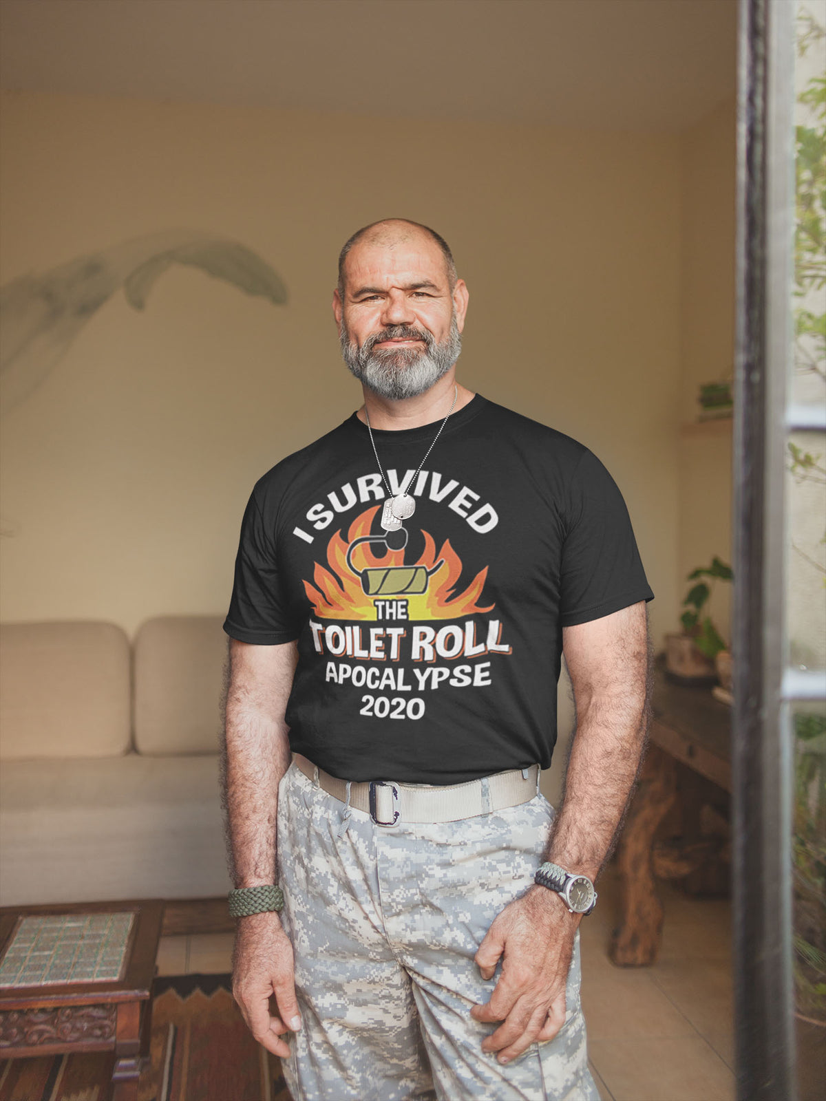 Man wearing 'I Survived The Toilet Roll Apocalypse 2020' t-shirt, showcasing a humorous design, in a cozy living room.