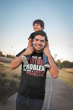 Man wearing Attitude Problem Funny Graphic Tee carrying child on shoulders outdoors.