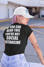 Woman wearing 'If You Can Read This You're Not Social Distancing On Back' t-shirt, showcasing humorous social distancing message.