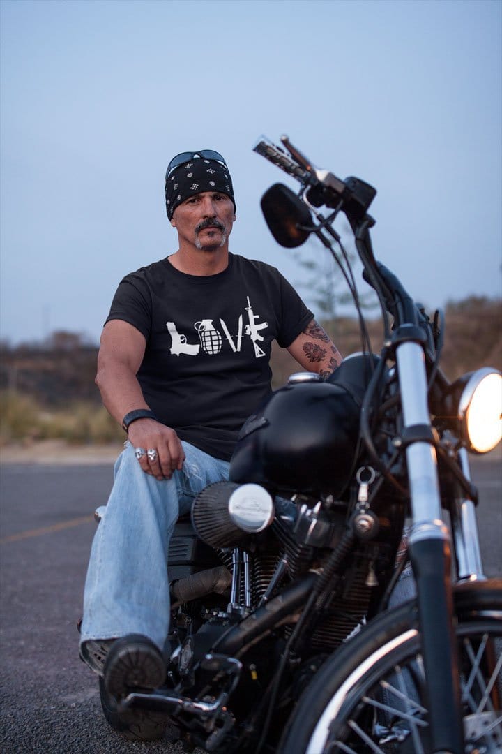 Man wearing Love As Pistol Grenade Knives And AR-15 shirt on a motorcycle