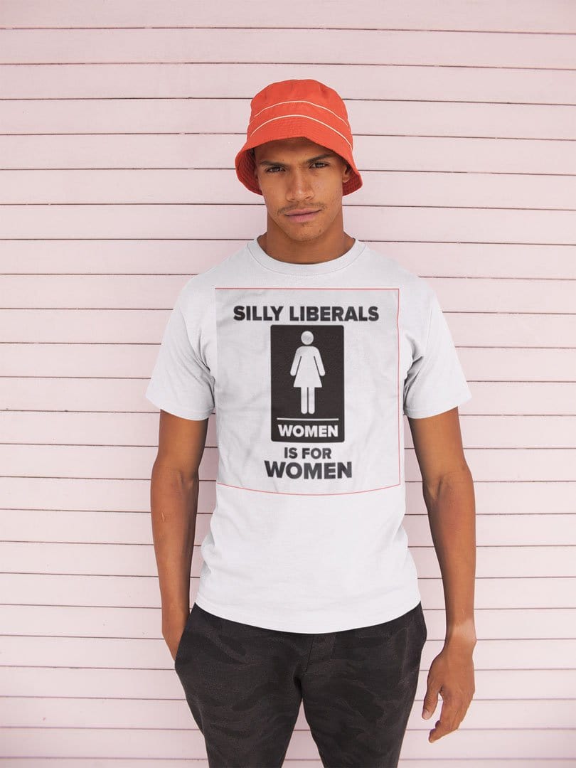 Man wearing a t-shirt with Silly Liberals Women Is For Women design, standing against a pink wall, casual fashion statement.