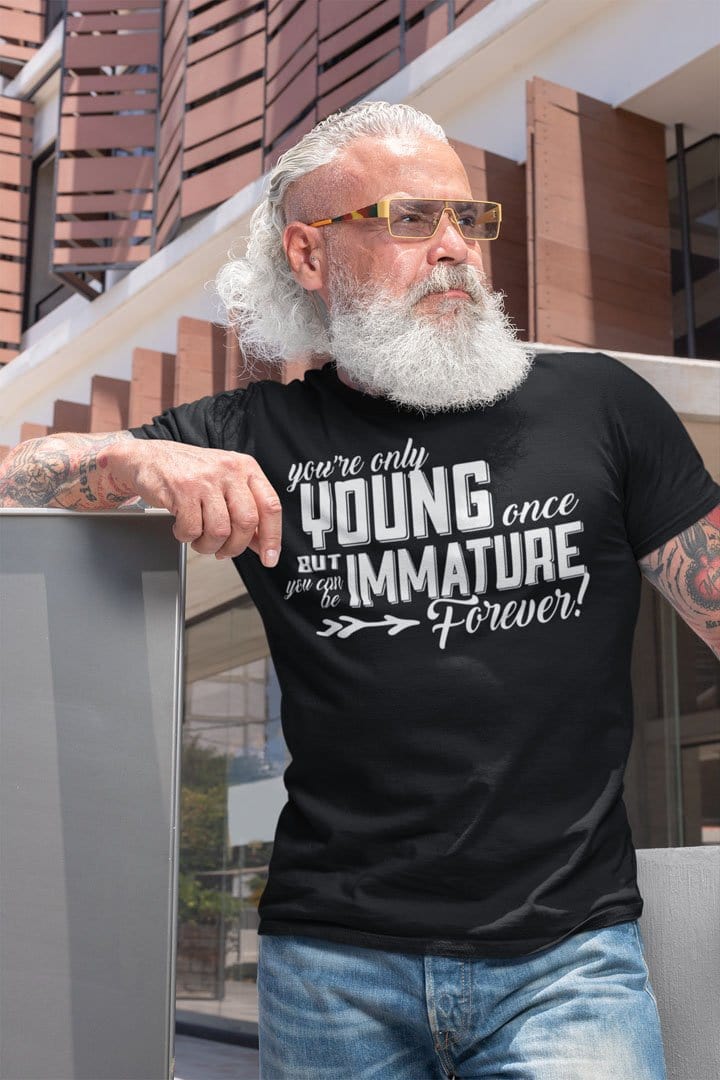 Man wearing 'Youth Fades Immature Stays Forever' graphic t-shirt outside modern building.
