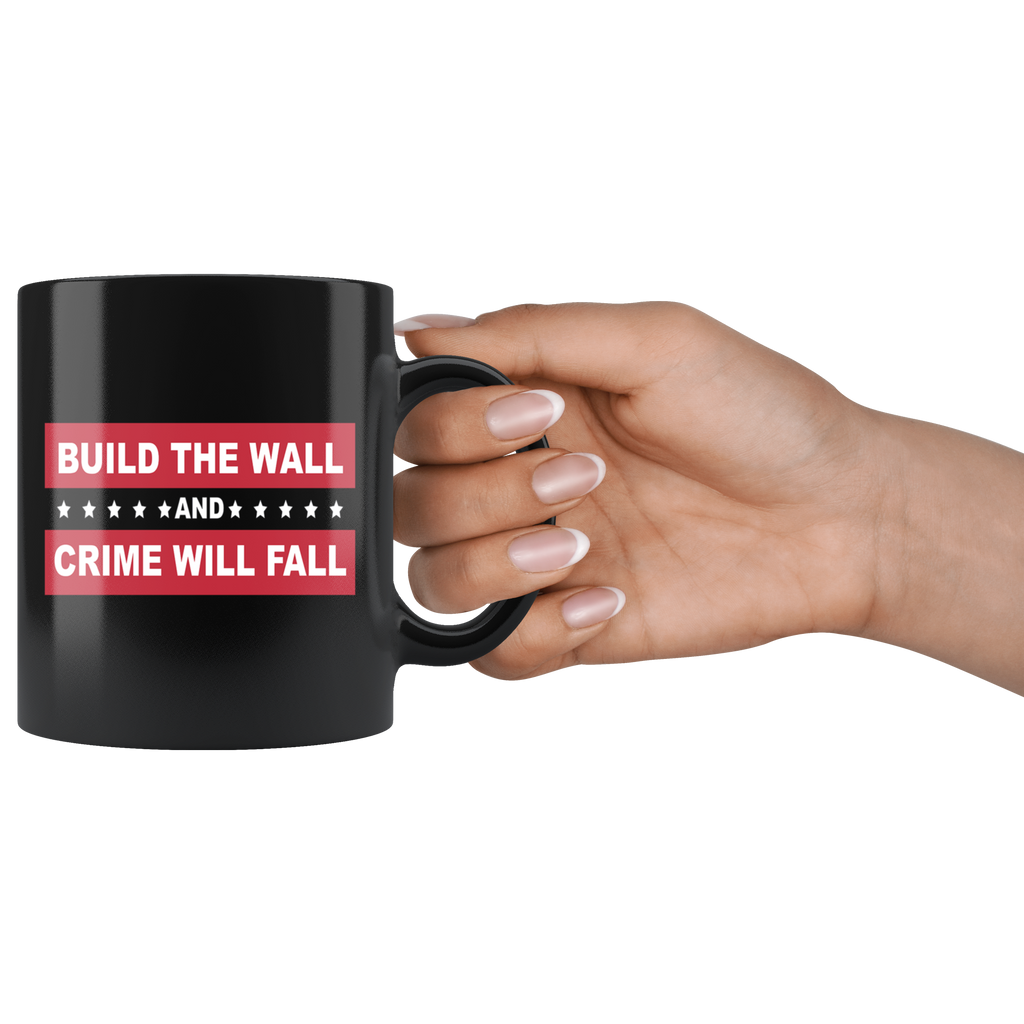 Border Security Equals Safer Land black mug held by hand, featuring "Build the Wall and Crime Will Fall" message, patriotic design
