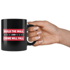 Border Security Equals Safer Land black mug held by hand, featuring "Build the Wall and Crime Will Fall" message, patriotic design