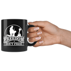 Hand holding black mug with Freedom Isn't Free Patriotic Graphic Tee design featuring a soldier and cross.