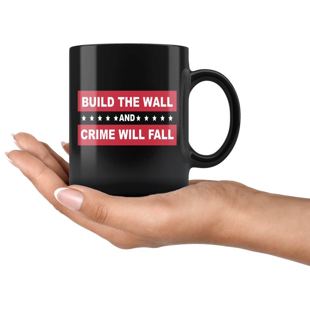 Hand holding Border Security Equals Safer Land black mug with 'Build The Wall And Crime Will Fall' text.